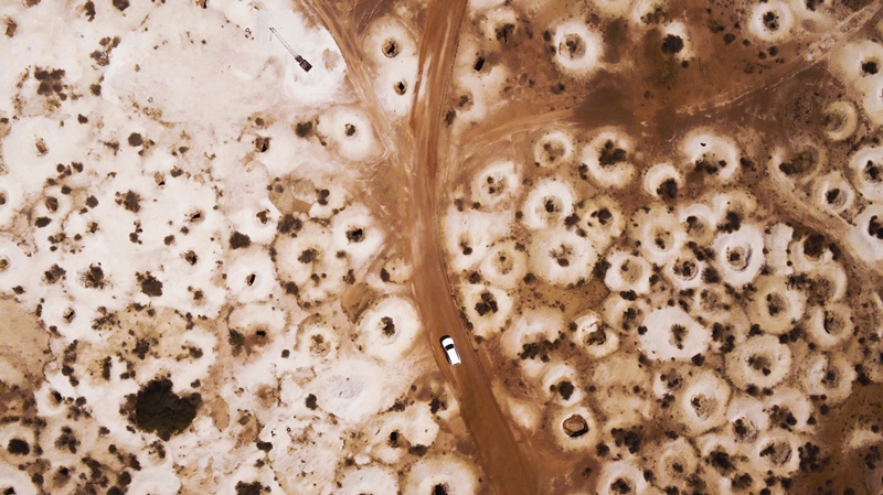 Aerial of a car driving through the outback town of White Cliffs