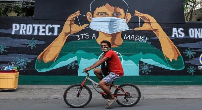 A man wearing a make-shift face mask passes by a mural urging people to wear face masks to prevent the spread of COVID-19 in Manila, the Philippines on April 14, 2021. (Xinhua/Rouelle Umali/IANS)