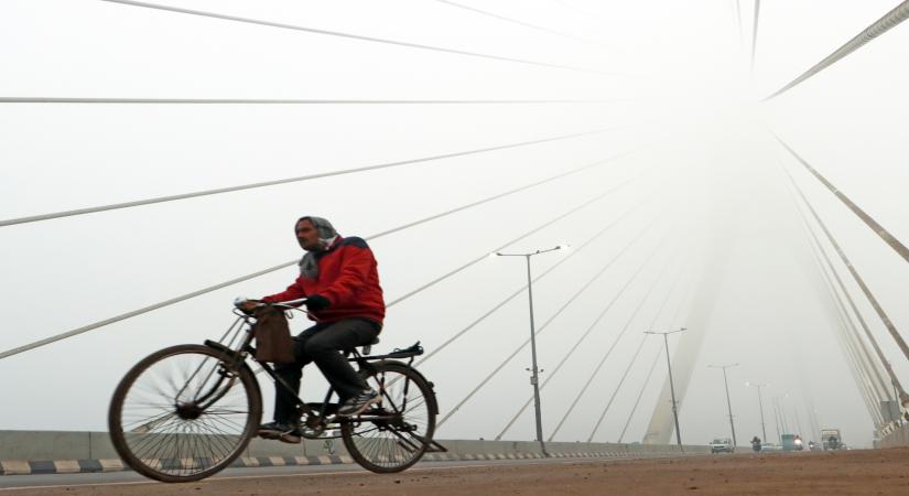 New Delhi: A man paddles the cycle as he passes through Signature bridge on a cold and foggy morning in New Delhi on Tuesday, December 27, 2022. (Photo: IANS/Wasim Sarvar)